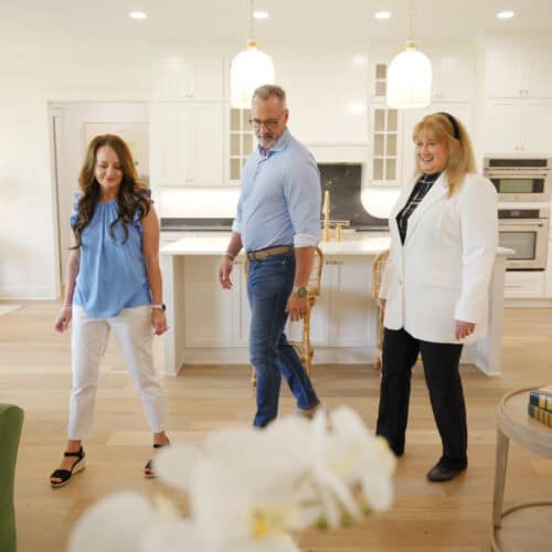 Elegant Modern Kitchen With White Cabinetry, Black Marble Countertops, And Stylish Pendant Lighting; Three People Inspecting Furniture Or Decor During A Home Visit In Tyler, Texas.