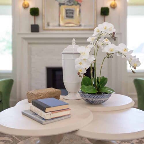 Elegant Living Room With White Coffee Table, Orchid Centerpiece, Green Armchairs, And Cozy Decorative Pillows In A Bright, Modern Setting.