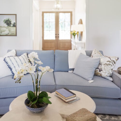 Elegant Living Room With A Light Blue Sofa, White And Floral Throw Pillows, And Fresh Flowers On Side Tables, Showcasing Stylish Furniture And Home Decor From Swann'S Furniture &Amp; Design In Tyler, Texas.