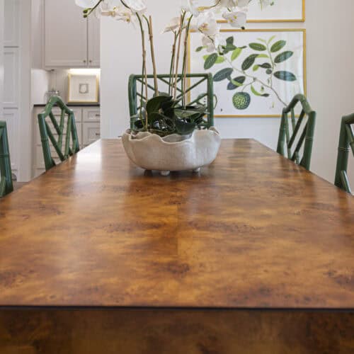 Handcrafted Wooden Dining Table With A Warm Finish, Surrounded By Stylish Green Bamboo-Style Chairs, In A Modern Dining Room Decorated With Botanical Art And A Floral Centerpiece.