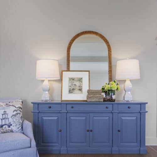 Elegant Blue Sideboard With Decorative Lamps, Framed Artwork, And Floral Arrangement, Complemented By A Large Wooden-Framed Mirror, Creating A Stylish And Inviting Interior Decor Setting.