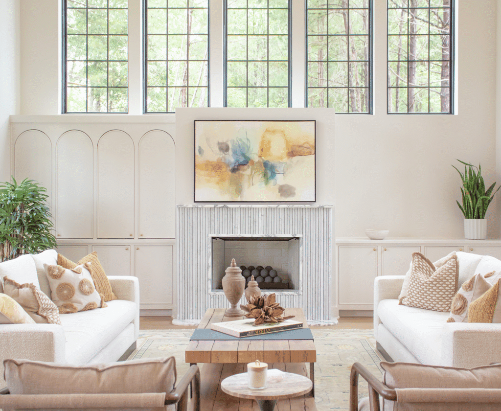 Elegant Living Room Interior Featuring A White Sofa With Decorative Pillows, A Fireplace With A Modern Mantel, Large Windows With Greenery View, Complemented By Stylish Decor And Indoor Plants For A Cozy, Sophisticated Ambiance.