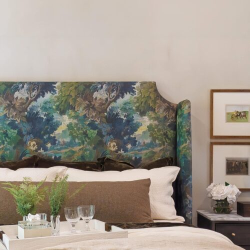 Luxurious Bedroom Featuring A Vibrant Floral Upholstered Headboard, Soft Bedding With Brown And White Pillows, Glassware On A Tray, And Artistic Framed Pictures On The Nightstand.