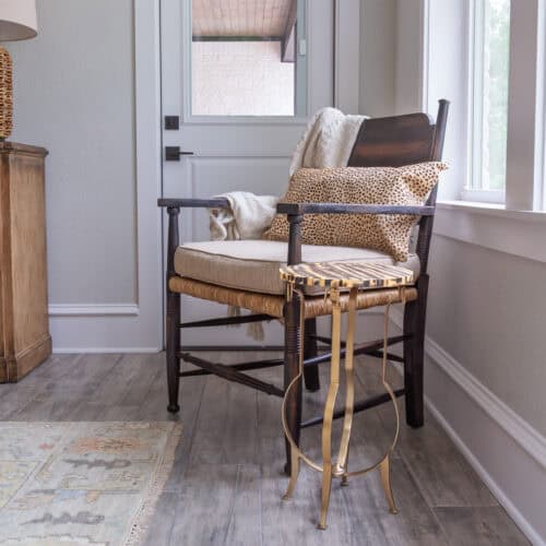 A Charming Wooden Chair With Plush Cushions And A Cozy Throw Blanket, Positioned Near A Window In A Bright, Inviting Room. A Stylish Side Table With A Decorative Metal Base Complements The Relaxing Co.