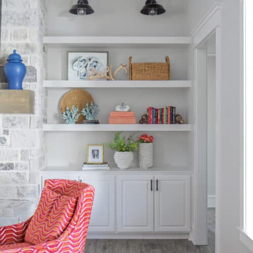 An Elegant White Built-In Bookshelf In A Bright, Modern Living Space, Decorated With Books, Vases, And Decorative Objects, Complemented By A Colorful Armchair.
