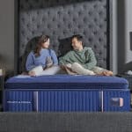 Comfortable couple sitting on a Reserve Firm Euro Pillow Top mattress in a modern bedroom setting.