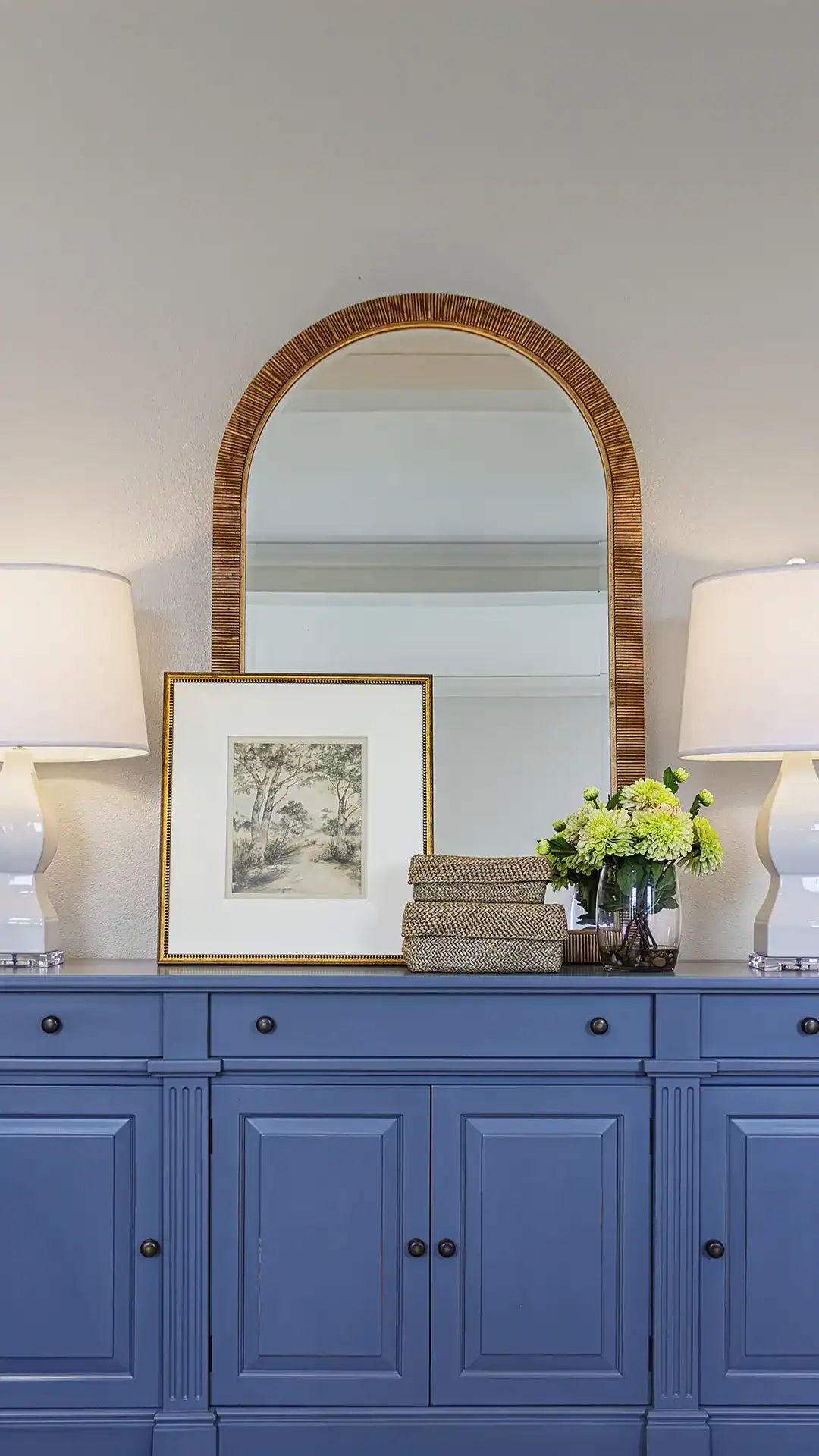 Stylish Blue Sideboard With Framed Artwork, Lamps, And Decorative Items In A Modern Interior Setting.