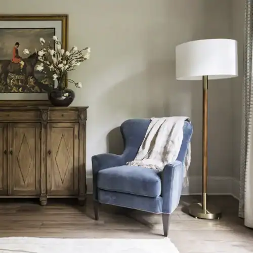 Stylish Blue Armchair With A White Throw Blanket, Positioned Next To A Tall Floor Lamp And A Wooden Sideboard In A Well-Lit, Inviting Space.