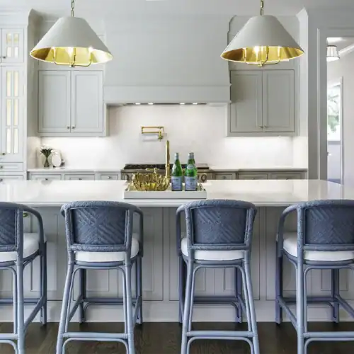 Bright Modern Kitchen Featuring A White Island With Blue Bar Stools, Pendant Lighting, And Sleek Cabinetry, Perfect For Contemporary Home Design.