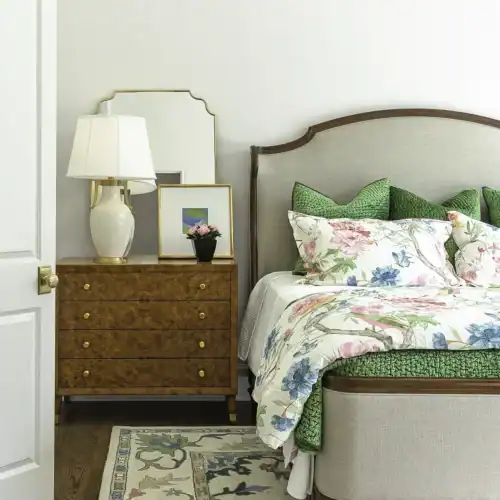 Cozy Bedroom Featuring A Vintage-Style Bed With Floral Bedding, A Wooden Nightstand With A Lamp, And A Colorful Area Rug, Showcasing Classic Interior Design.