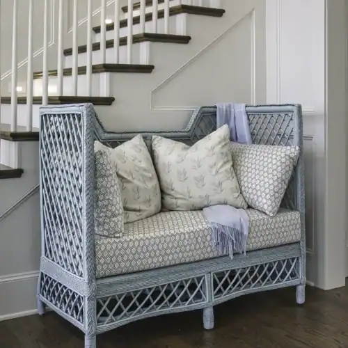 Stylish Blue Wicker Bench With Patterned Cushions And A Throw Blanket, Placed Under A Staircase In A Modern Home Interior.