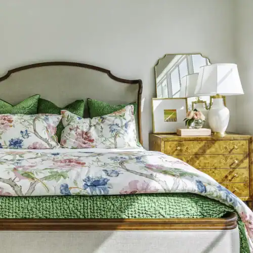 Beautiful Bedroom Featuring Floral Bedding, Green Accents, And A Wooden Dresser With A Mirror And Lamp, Showcasing Stylish Furniture From Swann'S Furniture &Amp; Design.
