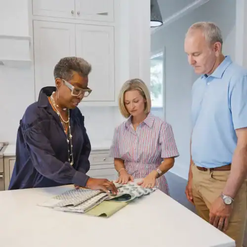 Three People Discussing Fabric Samples In A Modern Kitchen, Showcasing Interior Design And Furniture Selection At Swann'S Furniture &Amp; Design In Tyler, Texas.