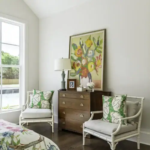 Bright And Airy Room Featuring White Chairs With Green Patterned Cushions, A Wooden Dresser, And Vibrant Artwork On The Wall, Showcasing Stylish Interior Design.
